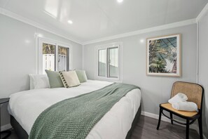Relax in this serene space with a large bed against a wall of windows, a wicker chair, and a beautiful artwork above.