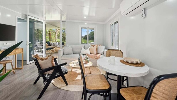A modern living room with a sofa, chairs, a coffee table, and a TV. - Leos Beach Hideaway, Stylish Tiny Home (Coffs Harbour)