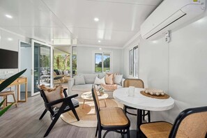 A modern living room with a sofa, chairs, a coffee table, and a TV. - Leos Beach Hideaway, Stylish Tiny Home (Coffs Harbour)