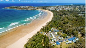 An aerial view of a coastal area with a beach, a small settlement with houses, and a road leading to the beach. - Leos Beach Hideaway, Stylish Tiny Home (Coffs Harbour)