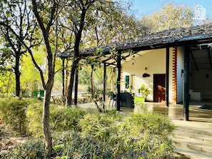 A covered outdoor area with a patio, seating, and a view of a building. - The Hideaway Hosur by evaddo stays (Hosur)