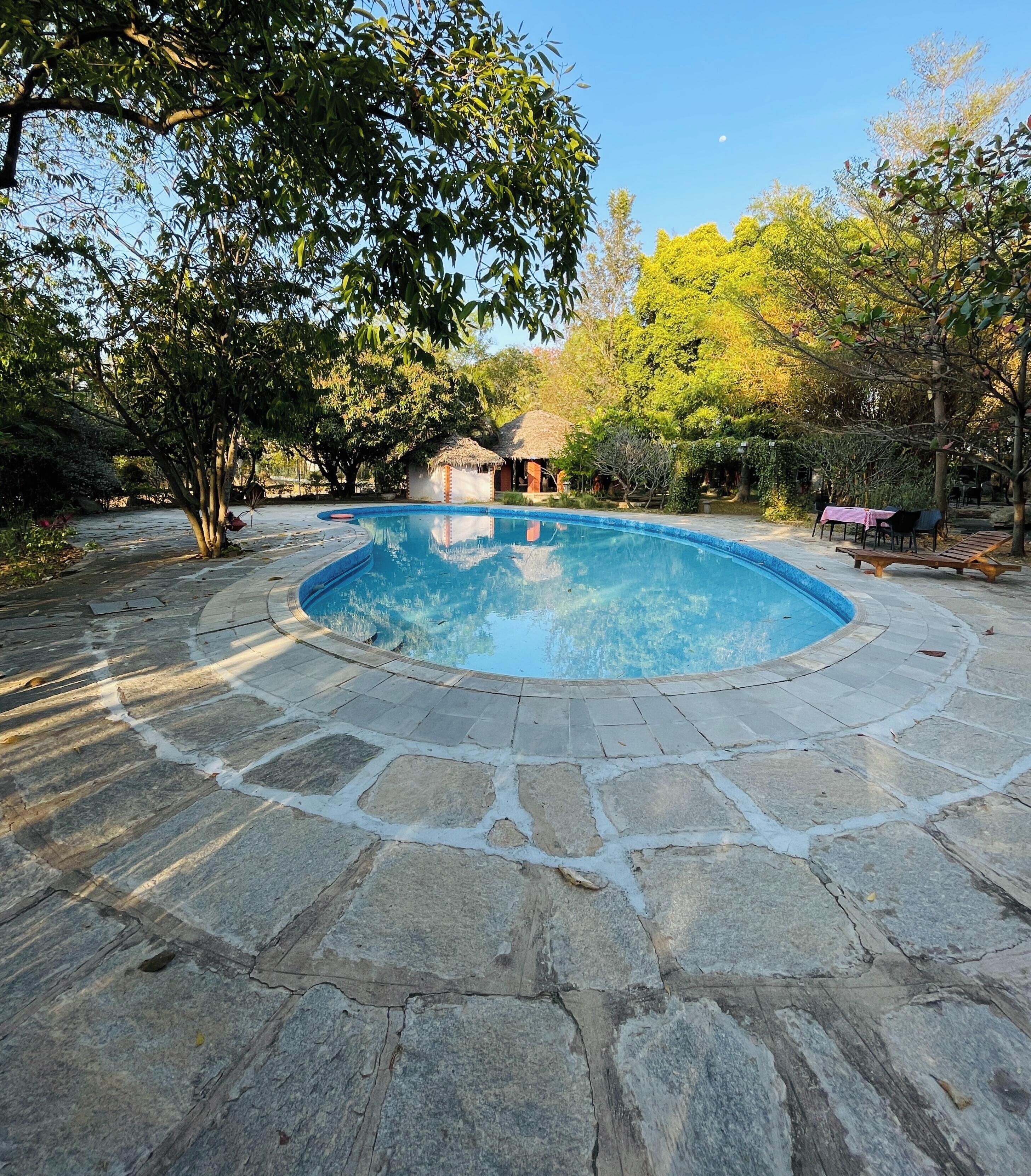 Una piscina con pavimento de piedra y una estructura de techo de paja al fondo.