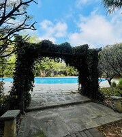 A stone pathway leading to a pool area with a view of a clear blue sky.