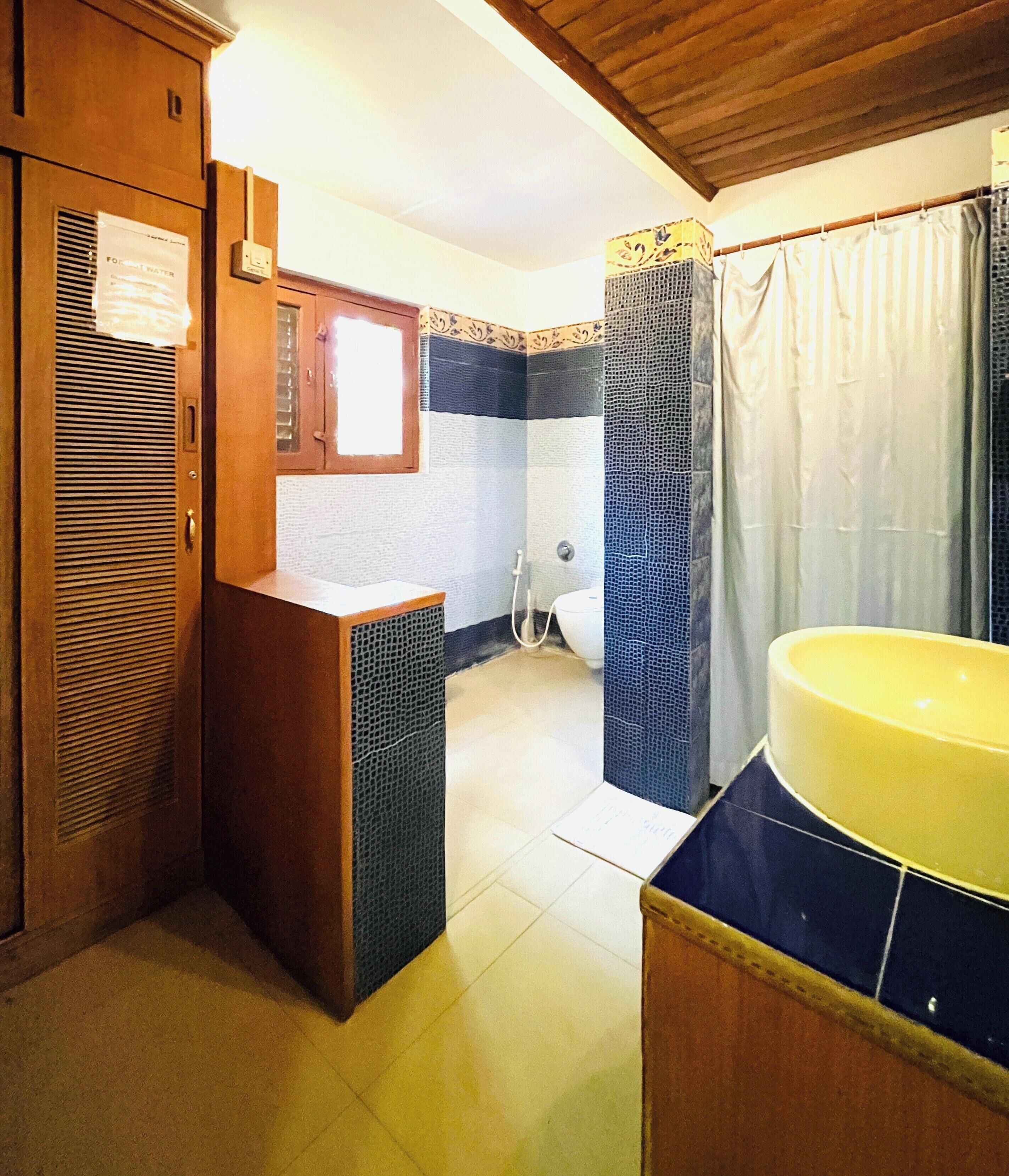 Un baño con tocador de madera, lavamanos amarillo y zona de ducha.