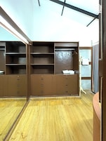 Una habitación con suelo de madera, un armario marrón con cajones y estantes, y una puerta con una toalla colgada.