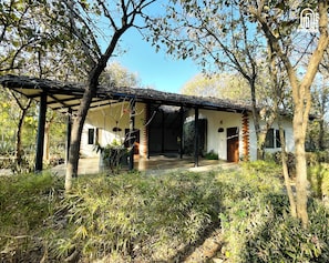 A traditional house with a covered porch, surrounded by trees and vegetation. - The Hideaway Hosur by evaddo stays (Hosur)