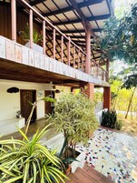 A covered outdoor area with a wooden balcony, potted plants, and a tiled floor.