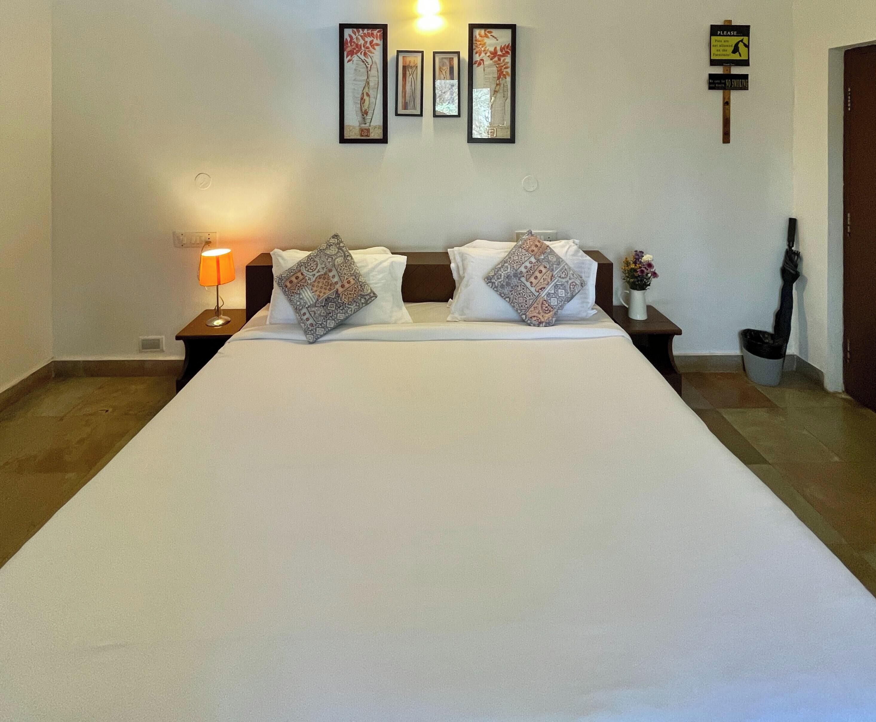 A hotel room with a large bed, two nightstands, a lamp, framed artwork on the wall, and a 'No Smoking' sign.