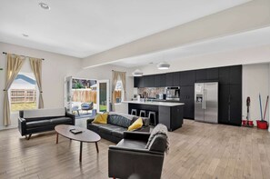 A modern living room with a sofa, coffee table, and a kitchen area with a refrigerator and cabinets.