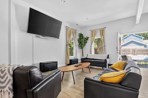 Ein modernes Wohnzimmer mit Flachbildfernseher, Ledersofas, einem Holztisch und Blick ins Freie.