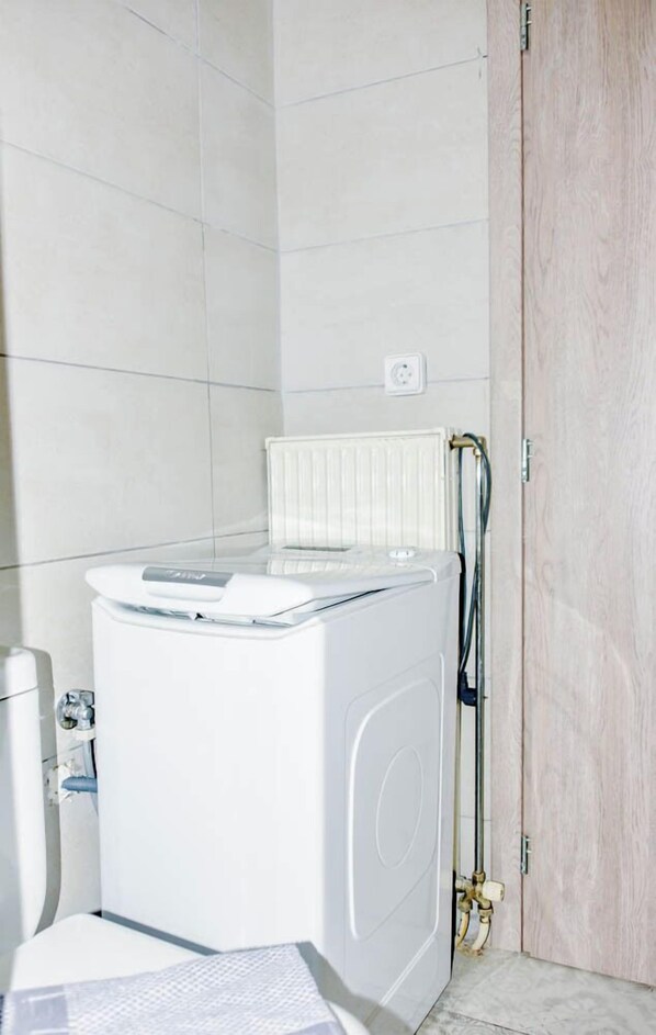 Een kleine, moderne wasruimte met een ingebouwde wasmachine en droger, een radiator en een houten deur.