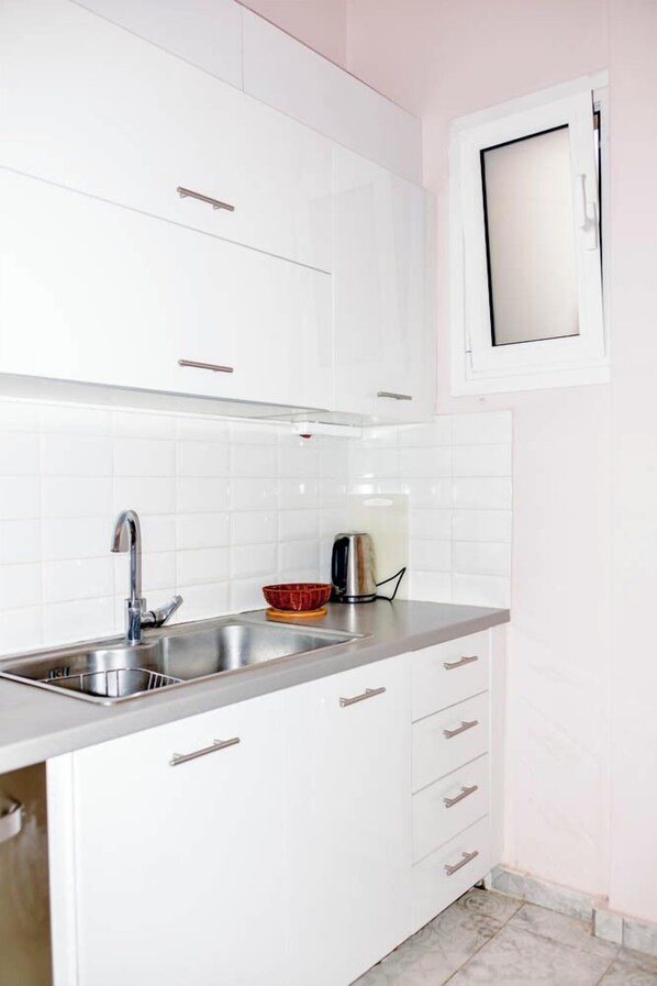 A kitchen with white cabinets, a stainless steel sink, and a window above the sink. - Acropolis view (Athens)