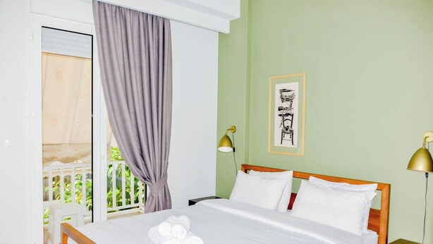 A hotel room with a wooden bed, white linens, a balcony with a view, and a framed artwork on the wall. - Acropolis view (Athens)