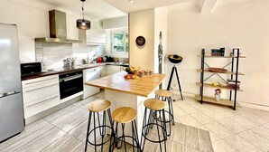 Una cocina moderna con una isla de madera, taburetes de bar, horno empotrado y estante metálico negro.