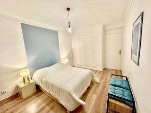 Un dormitorio con cama, lámparas de noche, un armario y un cuadro en la pared.