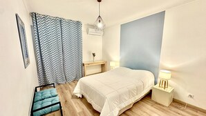 Un dormitorio con cama, mesitas de noche, una silla, una lámpara colgante y una ventana con cortinas estampadas.