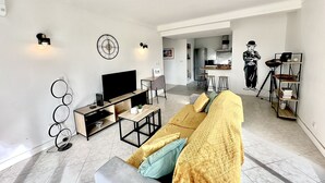 Una sala de estar moderna con un sofá, televisión y una cocina al fondo.