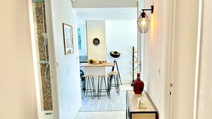 Un pasillo con piso de baldosas, una mesa de madera con un florero y una lámpara fijada en la pared.