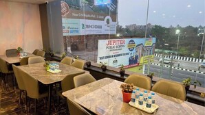 Un salón de conferencias con una pantalla grande mostrando un anuncio escolar, varias mesas con sillas y vistas a la ciudad a través de la ventana.
