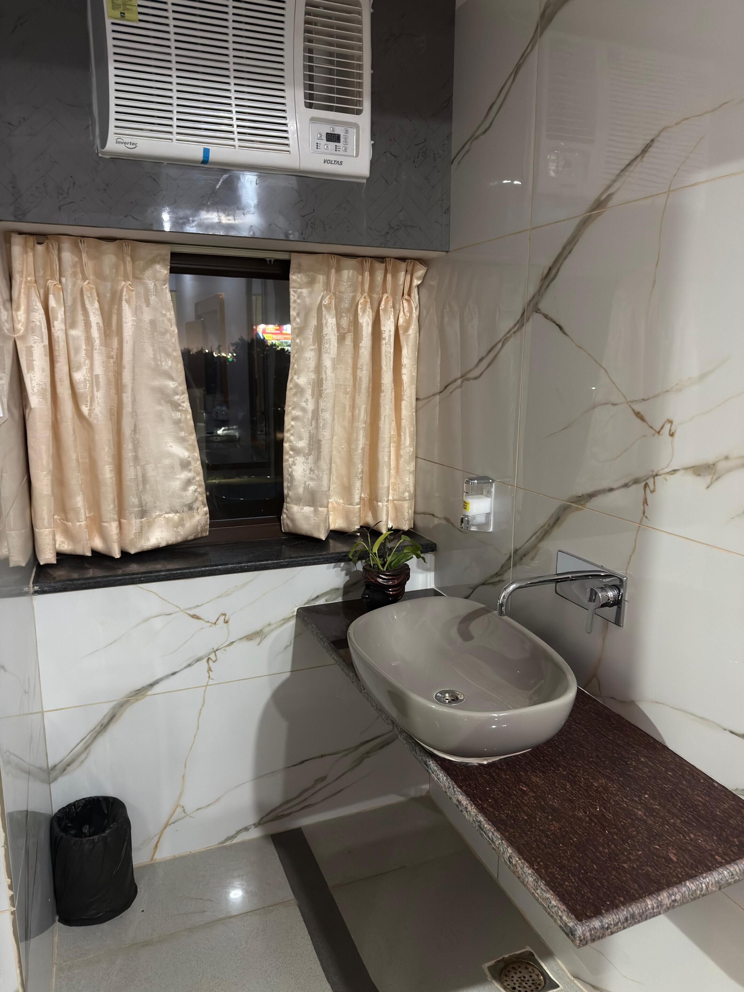 Un baño con lavamanos de mármol, una ventana con cortinas y un equipo de aire acondicionado.