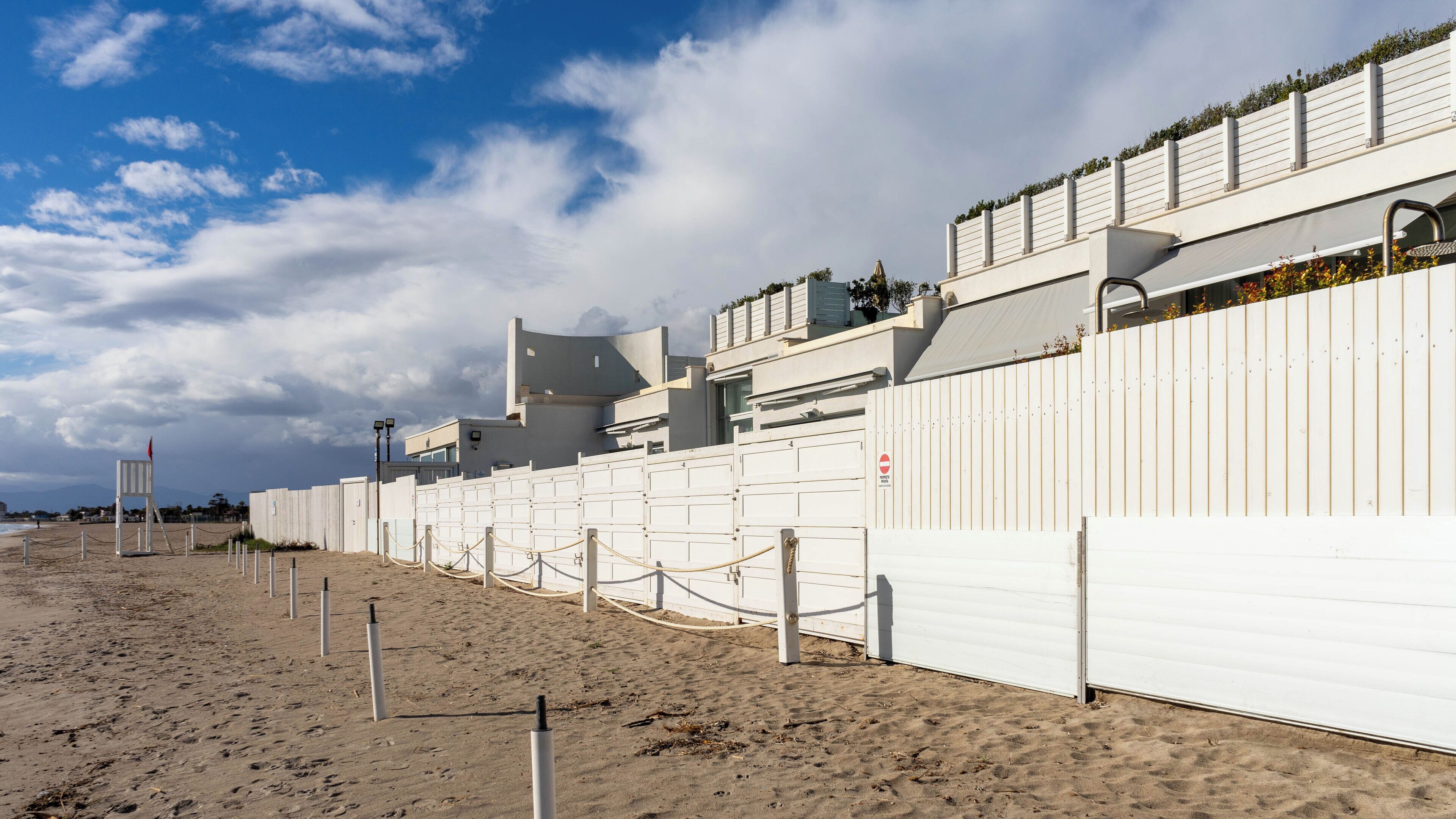 Une propriété située en bord de mer, avec une clôture blanche, un portail et un ciel dégagé.