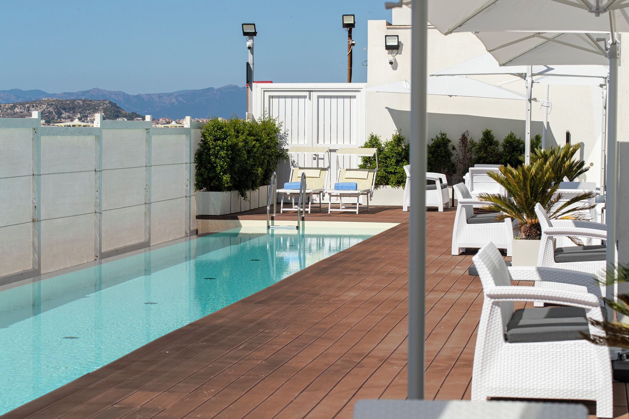 Une piscine sur le toit offrant une vue dégagée sur les montagnes en arrière-plan, des chaises longues blanches et une terrasse en bois.