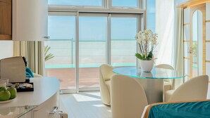 A modern hotel room with a glass table, comfortable seating, a view of the beach, and a balcony with a sliding door. - New Bussola (Quartu Sant'Elena)