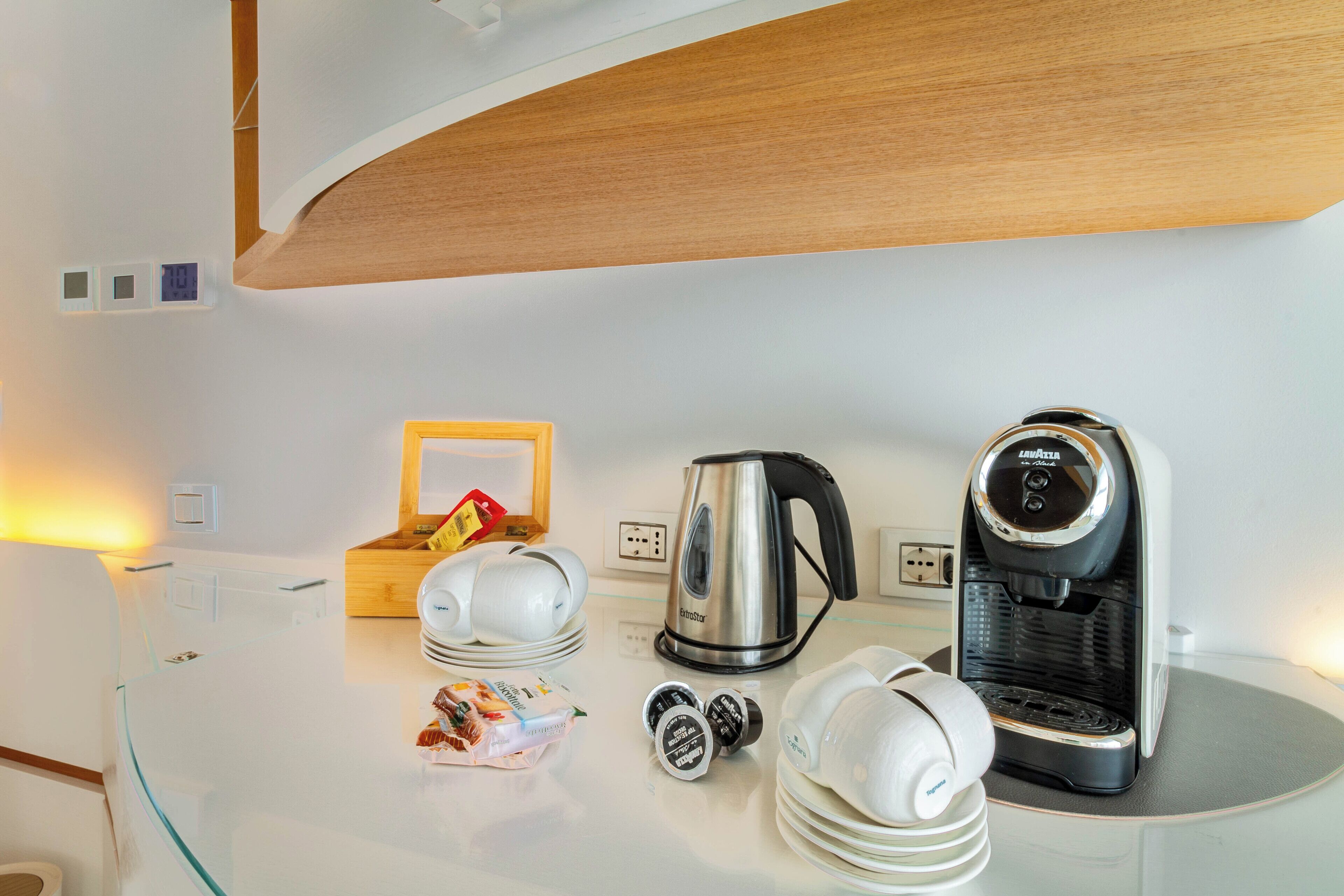 A modern kitchen with a coffee maker, kettle, and various kitchenware on a glass countertop.