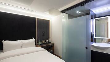 Ein modernes Hotelzimmer mit einem Bett, einem Nachttisch und einem vom Rest des Raumes abgetrennten Badezimmer mit Waschbecken und Spiegel.