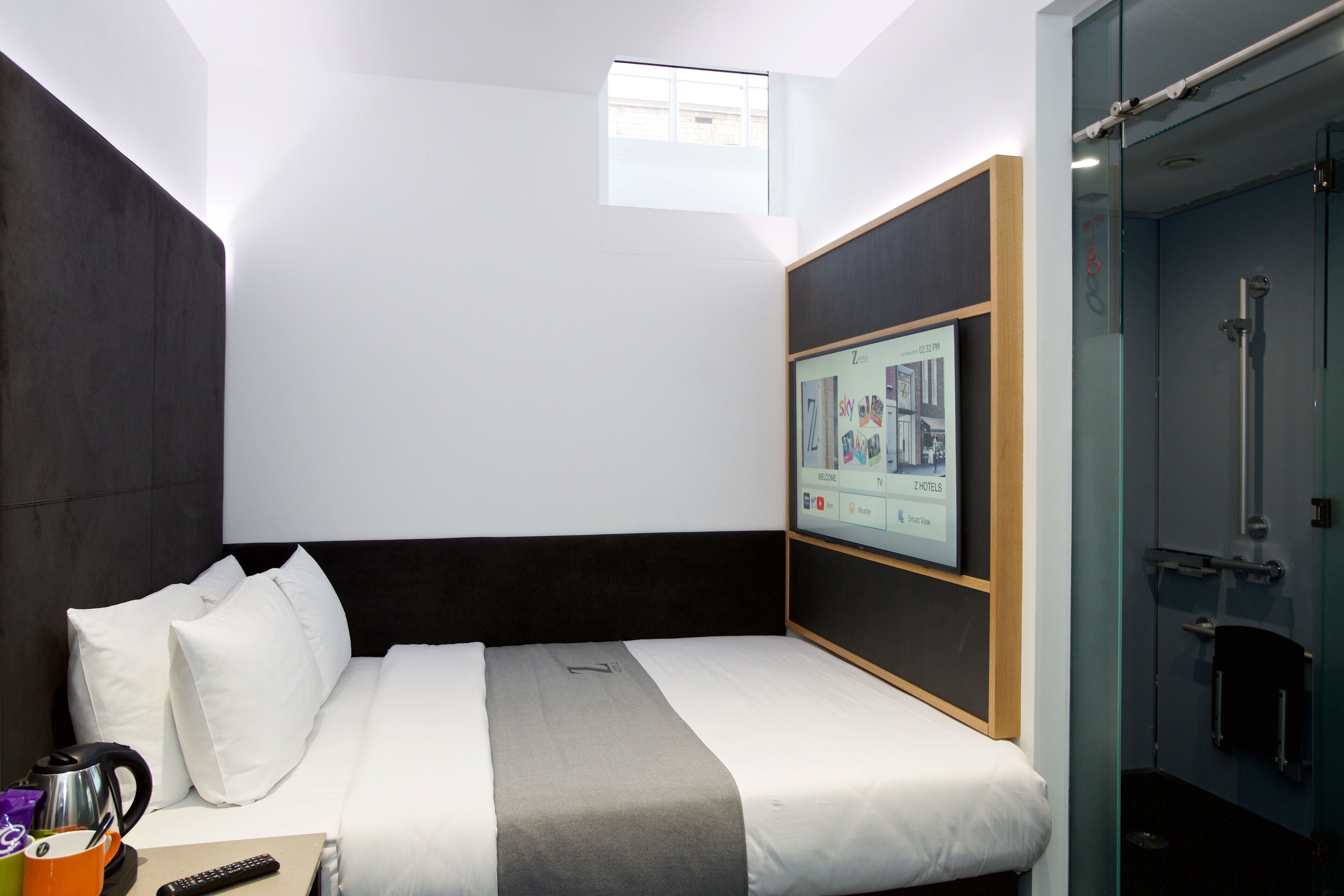 Ein Hotelzimmer mit Bett, Wandfernseher, Fenster und Duschbereich.
