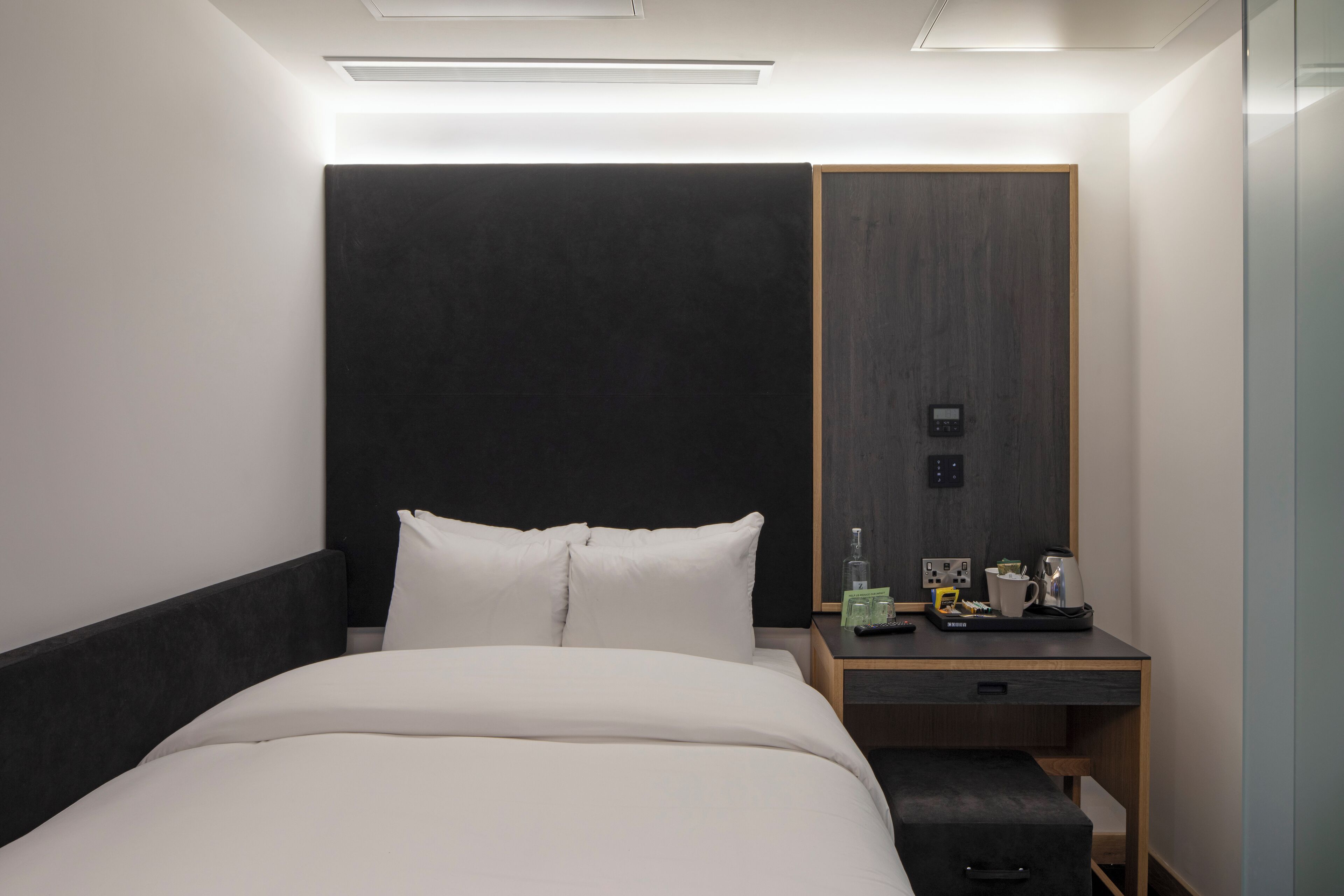 Ein modernes Hotelzimmer mit einem großen Bett, einem Nachttisch mit Lampe, einem kleinen Schreibtisch und einem Kleiderschrank.