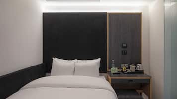Ein modernes Hotelzimmer mit einem großen Bett, einem Nachttisch mit Lampe, einem kleinen Schreibtisch und einem Kleiderschrank.