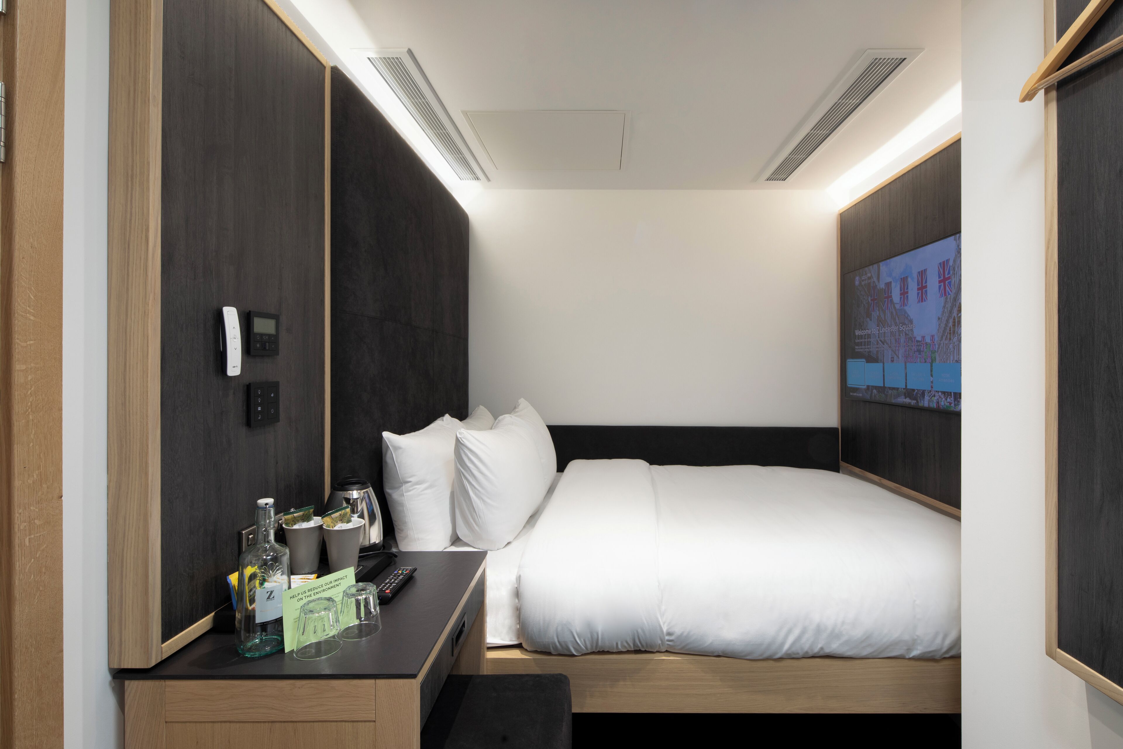 A modern hotel room with a bed, bedside table, and a TV screen displaying a cityscape.