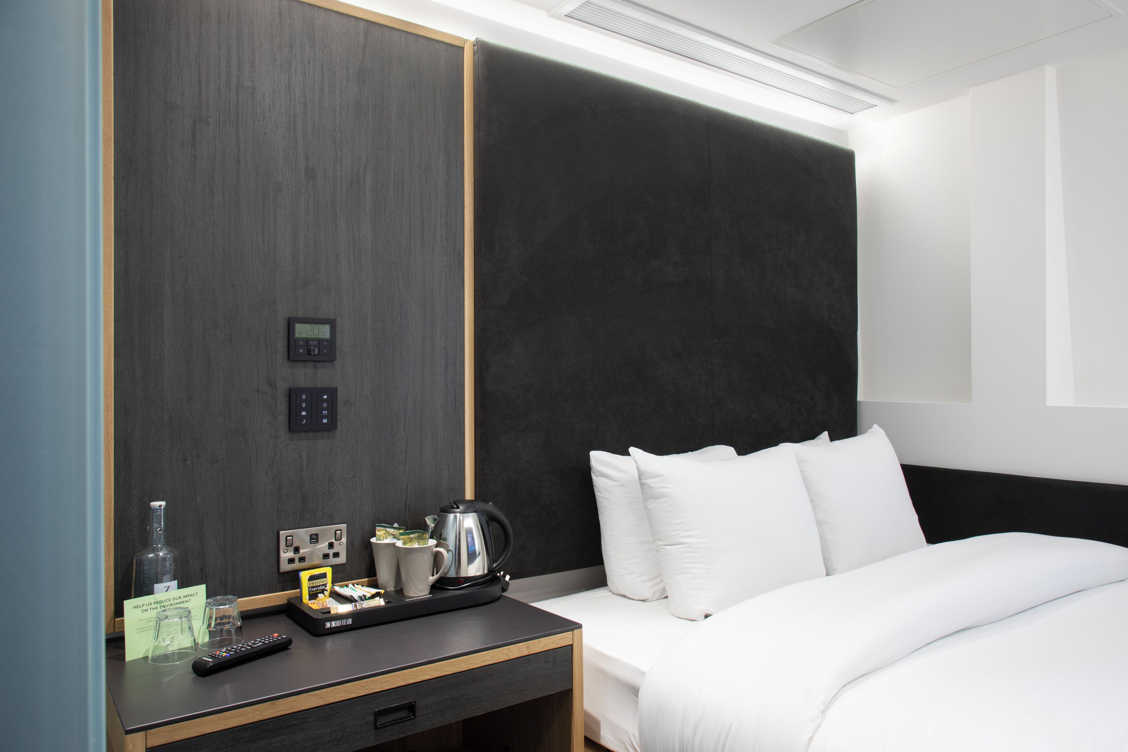 Ein Hotelzimmer mit Bett, Nachttisch und Bedienfeld an der Wand.