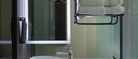 A modern bathroom with a large mirror, a white sink, and a towel rack with folded towels.
