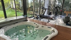 Un jacuzzi en una habitación con suelo de madera, ventanas amplias y equipo de ejercicio.