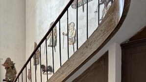 Una escalera con barandilla curva, una puerta de madera y suelo de baldosas.