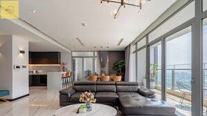 A modern living room with a sectional sofa, a round coffee table, and a view of the city through large windows. - Landmark 81 Magical Tower Apartment (Ho Chi Minh City)