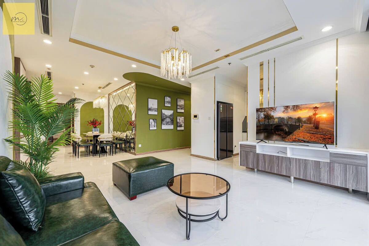 A modern living room with a green accent wall, a large flat-screen TV, and a glass coffee table.