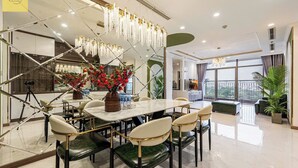 A modern dining area with a marble table, green upholstered chairs, and a floral centerpiece. - Landmark 81 Magical Tower Apartment (Ho Chi Minh City)