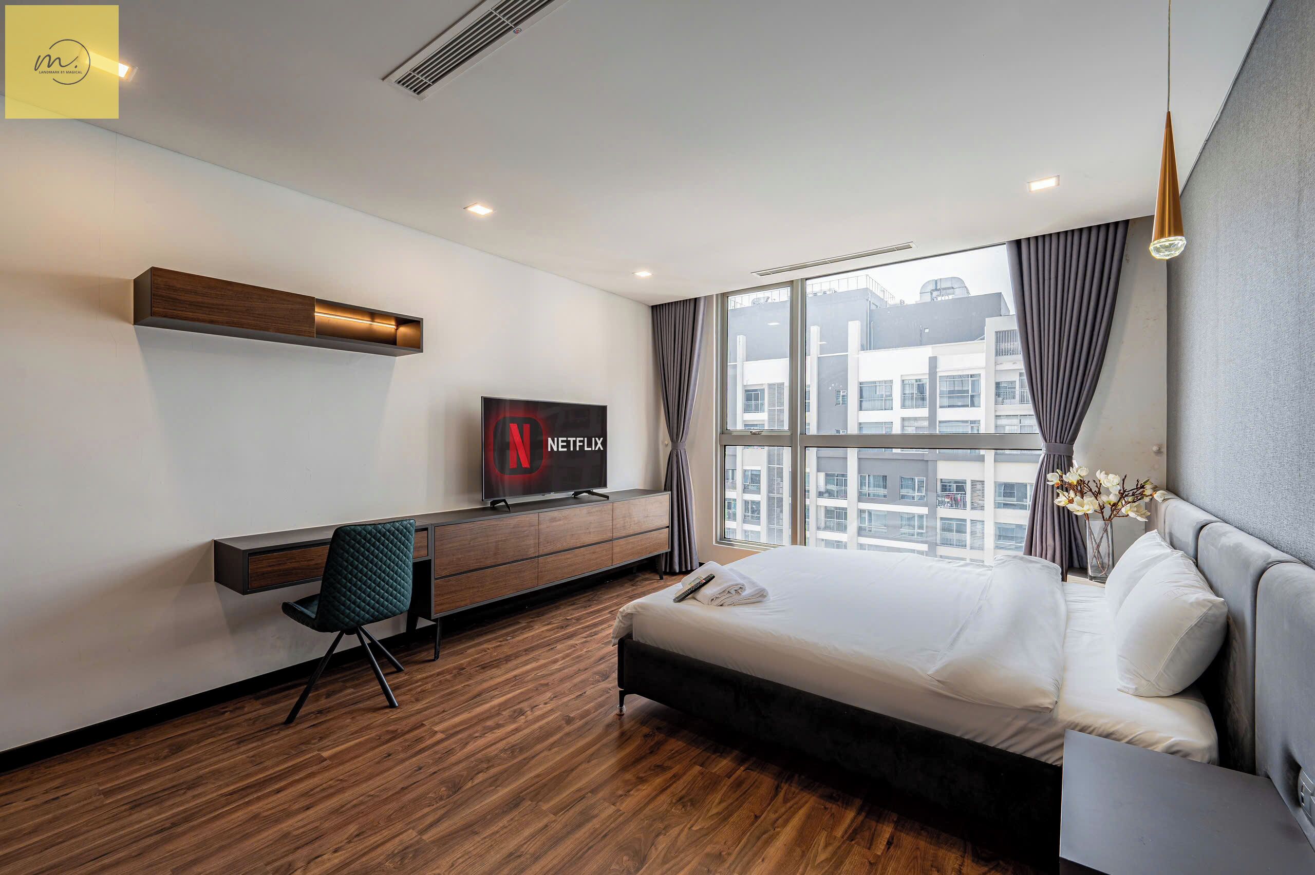 A modern hotel room with a large bed, a desk with a chair, a TV, and a window with curtains.