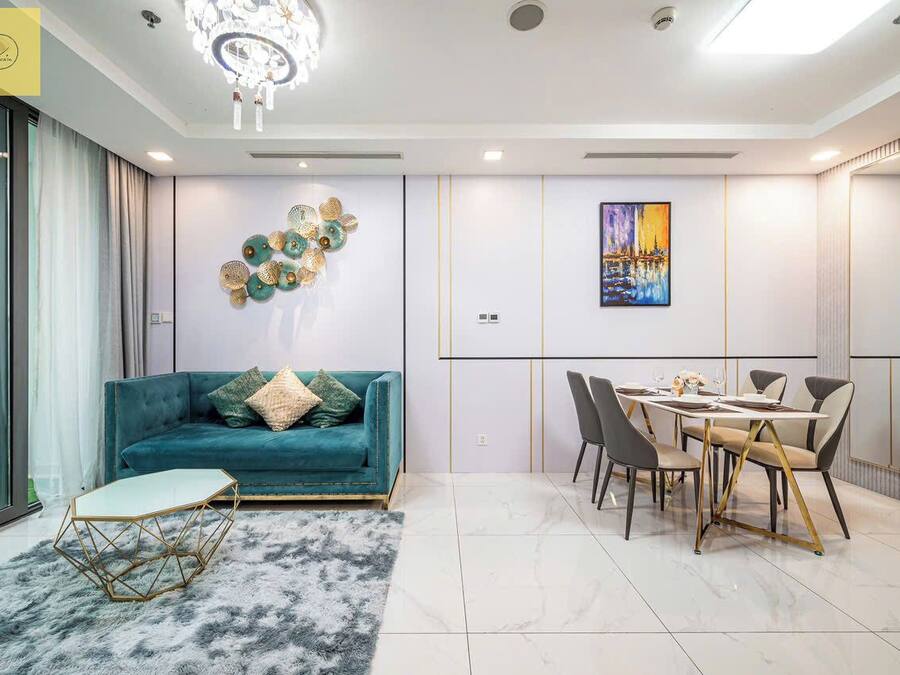 A modern living room with a teal sofa, a dining table with chairs, and a chandelier.