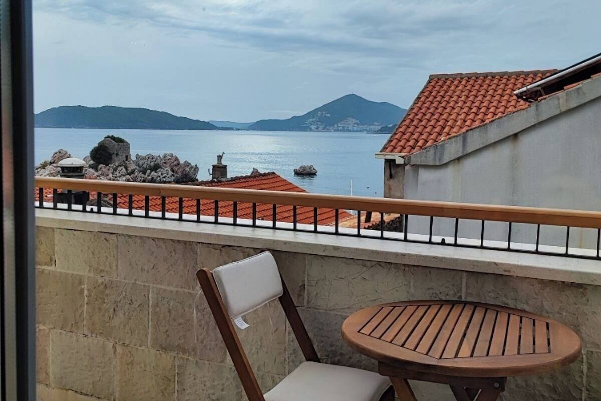 A balcony with a table and two chairs, overlooking a body of water and distant mountains.