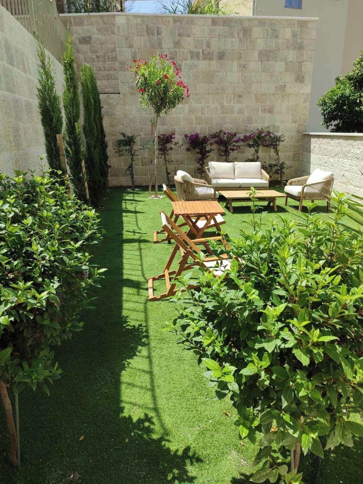 A patio with a stone wall, green artificial grass, and outdoor furniture including a sofa and chairs.