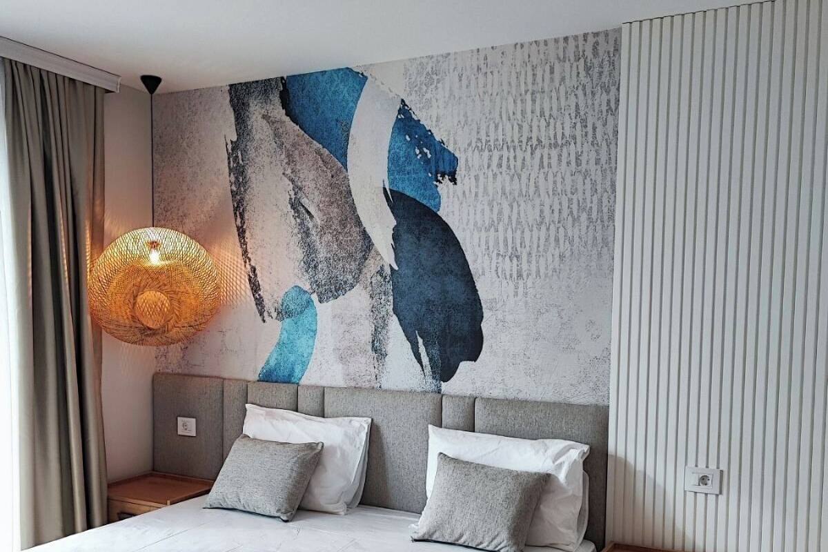 A modern bedroom with a large bed, a nightstand, a bedside table, and a wall-mounted lamp.