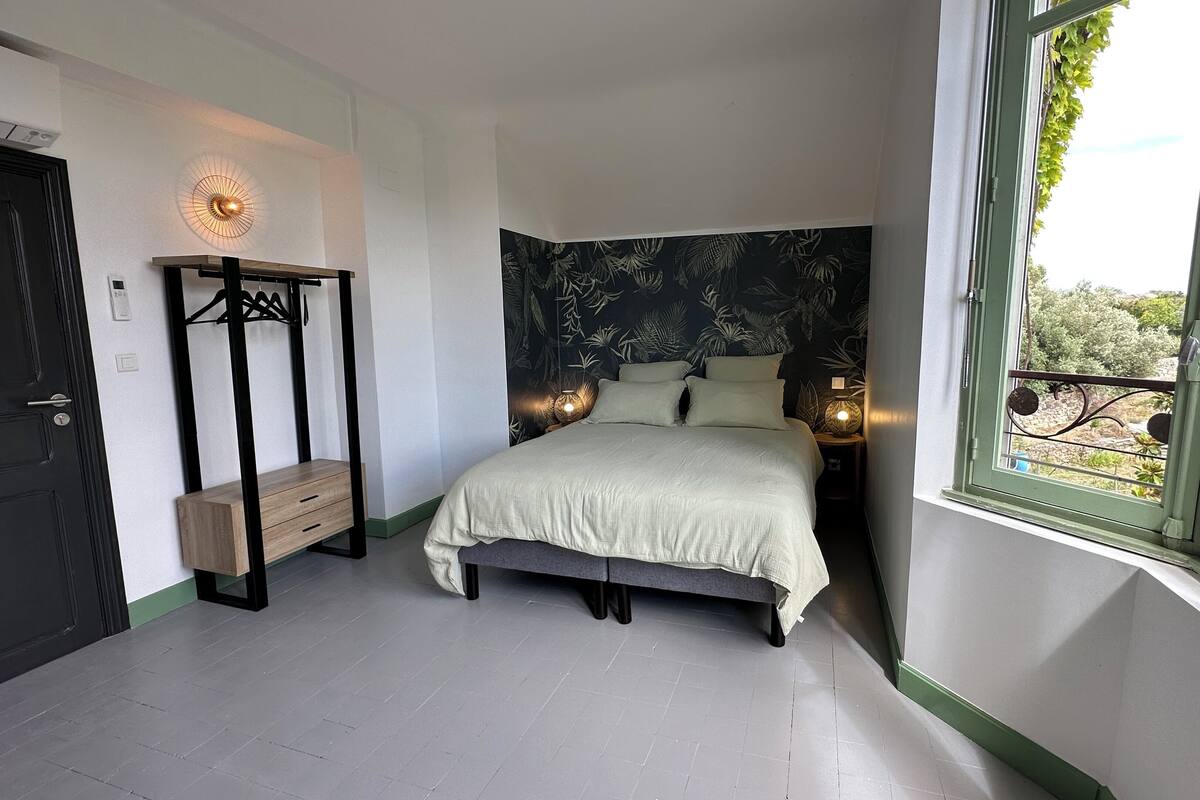 Un dormitorio con cama, mesita de noche con lámparas, armario y ventana con vistas.