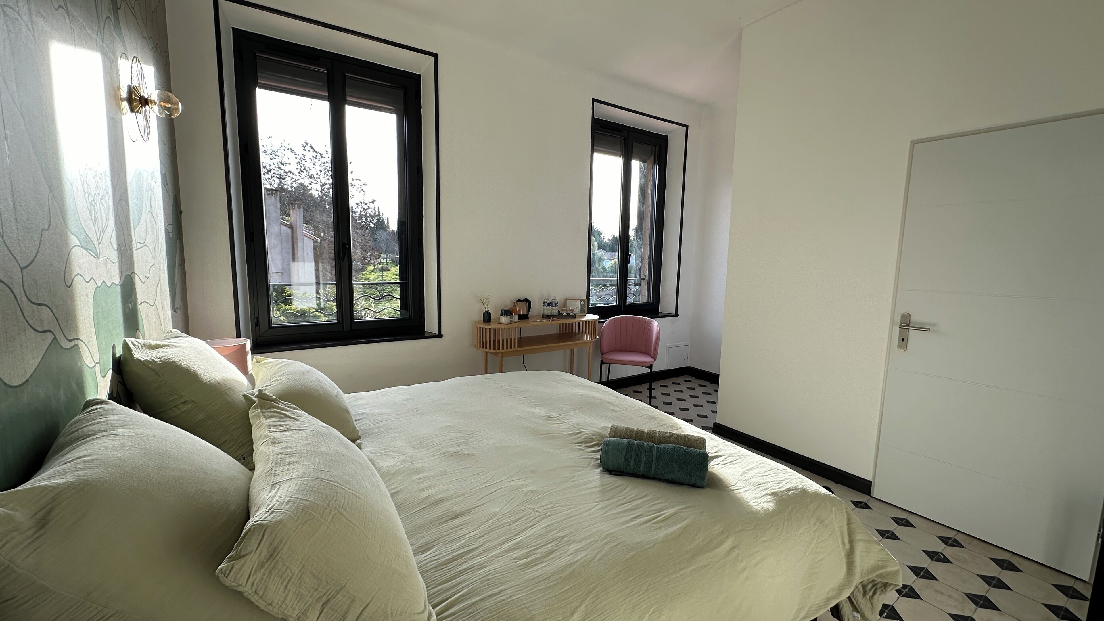 Een slaapkamer met een bed, twee ramen, een bureau, een stoel en een deur.