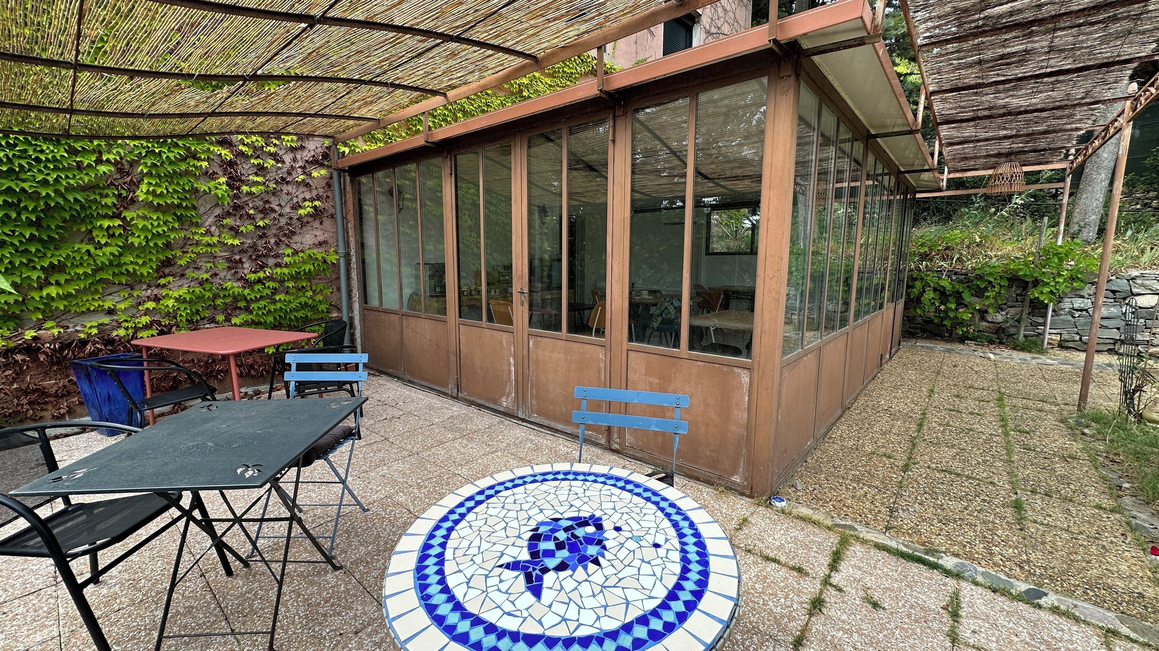 A covered patio area with a mosaic table, a red table, and blue benches.