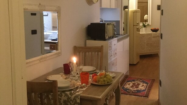 A dining area with a table set for two, a clock on the wall, and a kitchen in the background. - LOFT - TOLOMEI Residence - Sacile (Sacile)
