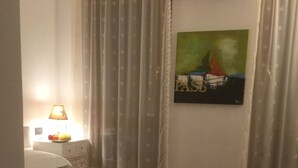 A bedroom with a bed, a nightstand, a lamp, a painting, and sheer curtains. - LOFT - TOLOMEI Residence - Sacile (Sacile)